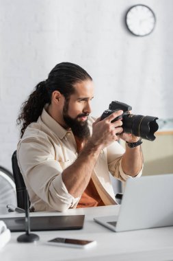 Latin fotoğrafçı ev stüdyolarındaki bulanık aletlerin yanında dijital kamerada fotoğraf çekiyor.