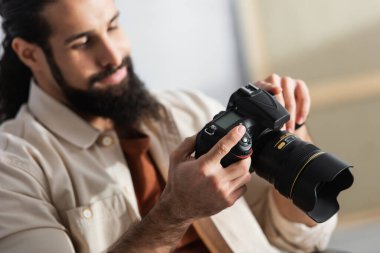 Evde çalışırken dijital fotoğraf makinesi tutan bulanık Latin fotoğrafçı.