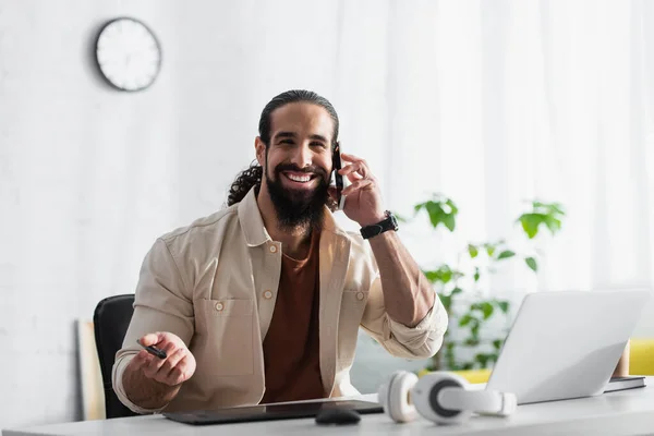 Lächelnder Designer Spricht Auf Handy Der Nähe Von Verschwommenem Laptop — Stockfoto