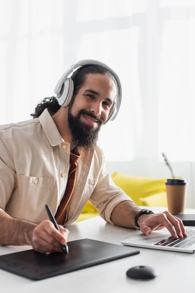 Lächelnder Hispanischer Designer Mit Kopfhörern Der Laptop Arbeitet Und Hause lizenzfreie Stockfotos