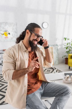 Oturma odasında akıllı telefondan konuşurken gülümseyen İspanyol adam dikkat çekiyor.