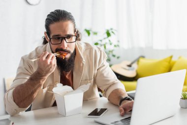 Sakallı İspanyol serbest çalışan akıllı telefon kullanıyor ve evde Çin eriştesi yiyor.