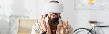 VR kulaklıklı, şaşkın İspanyol adam evde oynarken yaptığı jestleri gösteriyor.