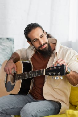 Sakallı İspanyol müzisyen evde akustik gitar çalıyor.