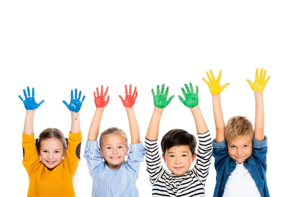 Fröhliche multiethnische Kinder mit Händen in bunter Farbe, die isoliert auf weiß in die Kamera schauen — Stockfoto