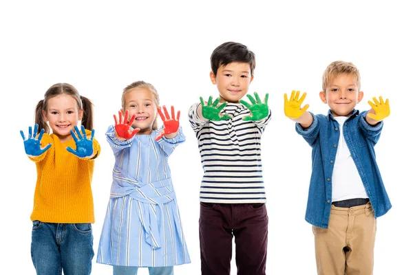 Crianças multiétnicas sorrindo enquanto mostram mãos bagunçadas em tinta colorida isolada em branco — Fotografia de Stock