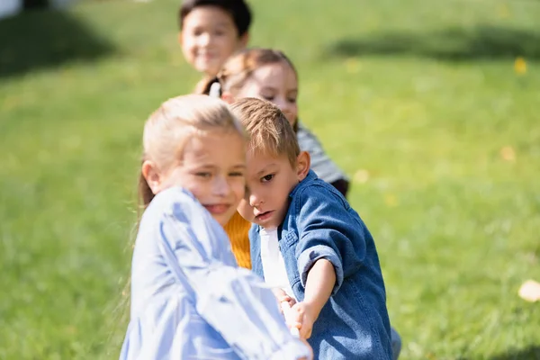 Ragazzo tirando corda mentre gioca tiro alla fune con gli amici in primo piano sfocato nel parco — Foto stock