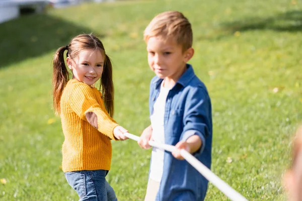 Positives Kind spielt Tauziehen mit Freund auf verschwommenem Vordergrund im Park — Stockfoto