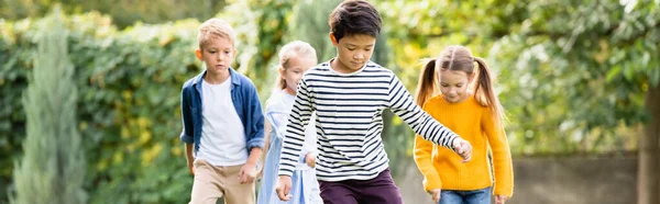 Asiático chico corriendo cerca amigos en borrosa fondo en parque, bandera — Stock Photo
