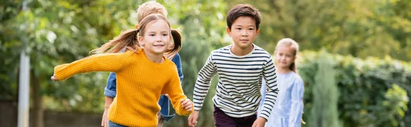 Lächelndes Mädchen läuft neben multiethnischen Freunden im Park, Transparent — Stockfoto