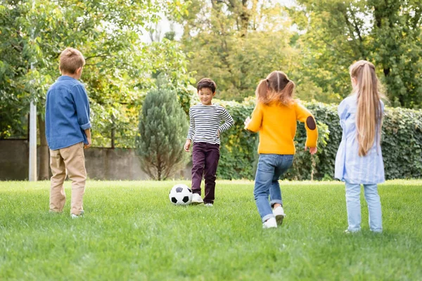 Fröhlicher asiatischer Junge spielt mit Freunden Fußball auf Rasen — Stockfoto