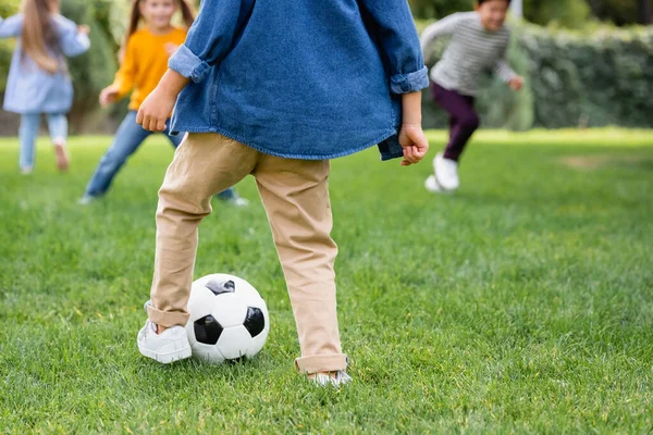 Мальчик играет в футбол с друзьями на размытом фоне на лужайке — стоковое фото