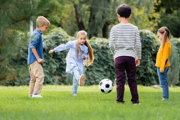 Дівчина грає в футбол з друзями на розмитому передньому плані в парку — стокове фото