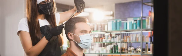 Friseur in Latexhandschuhen und Gesichtsschutz schneiden Haare des Mannes in medizinischer Maske, Banner — Stockfoto