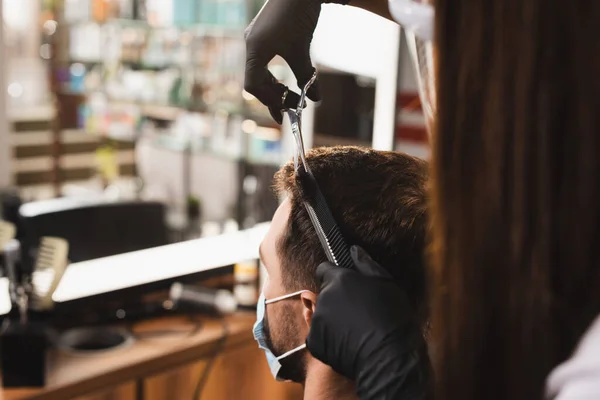 Парикмахер в латексных перчатках стрижет волосы клиента в медицинской маске — стоковое фото