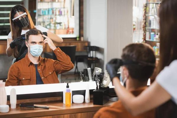 Spiegelbild des Friseurs im Gesicht Schild schneidet Haare des Mannes zeigt mit Fingern, verschwommener Vordergrund — Stockfoto
