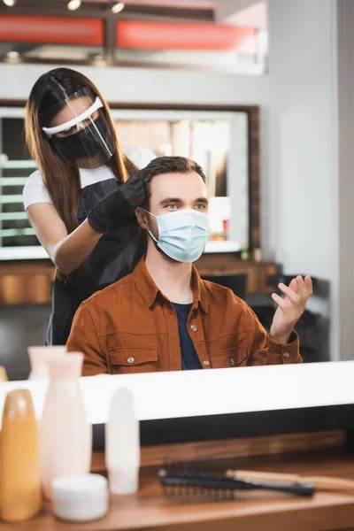 Miroir reflet de geste homme dans le masque médical et coiffeur dans le bouclier facial couper ses cheveux — Photo de stock