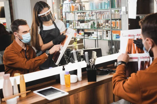 Specchio riflesso di parrucchiere e cliente guardando tavolozza dei colori dei capelli su primo piano sfocato — Foto stock