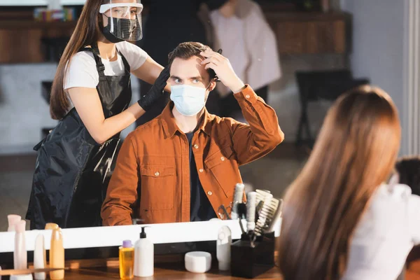 Дзеркальне відображення перукаря, який торкається волосся клієнта, розмитий передній план — стокове фото