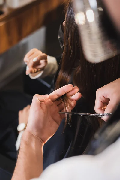 Mulher mostrando pouco gesto perto de cabeleireiro cortando seu cabelo no fundo borrado — Fotografia de Stock