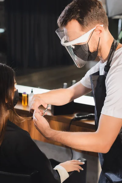 Peluquero en el escudo facial cortar el pelo de la mujer en máscara médica - foto de stock
