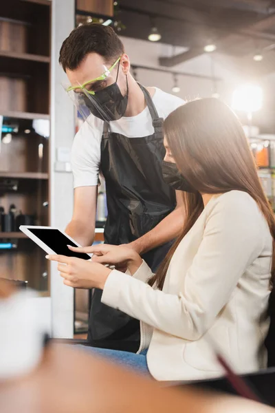 Hairdresser in face shield near woman using digital tablet, blurred foreground — Stock Photo