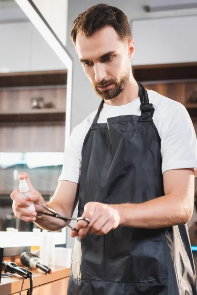 Young bearded hairdresser sanitizing scissors with disinfectant — Stock Photo