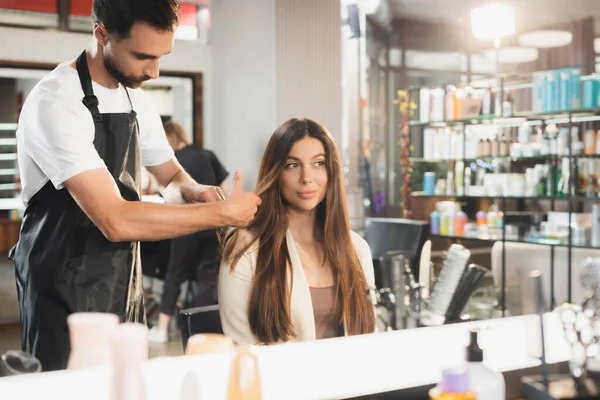 Miroir reflet de coiffeur peignage cheveux de jeune femme, avant-plan flou — Photo de stock