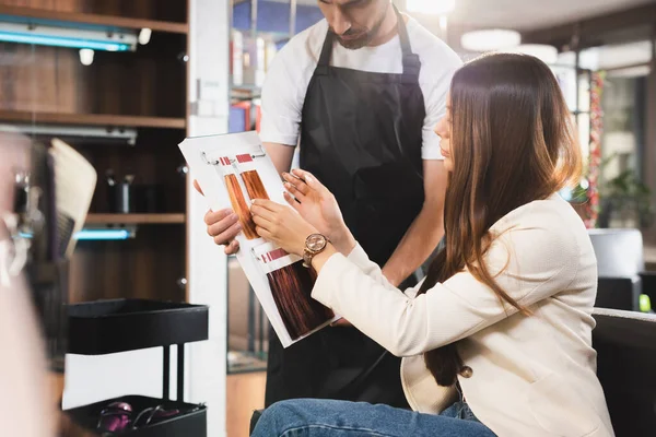 Hairdresser showing hair colors palette to client, blurred foreground — Stock Photo