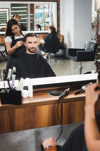 Espelho reflexo de barbeiro jovem corte de cabelo do homem barbudo, foreground borrado — Fotografia de Stock