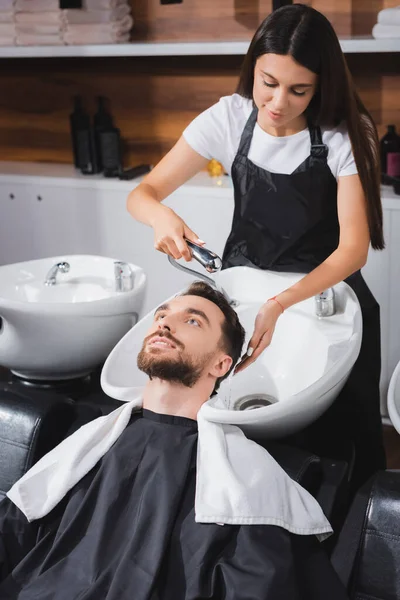 Junger Friseur wäscht im Schönheitssalon die Haare seiner Kundin — Stockfoto