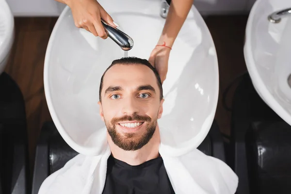 Вид сверху на парикмахера, моющего волосы улыбающегося мужчины — стоковое фото