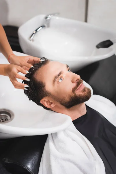 Peluquero lavado de cabello de hombre barbudo joven en salón de belleza - foto de stock