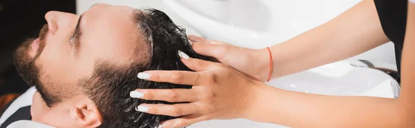 Hairdresser washing hair of young man in beauty salon, banner — Stock Photo