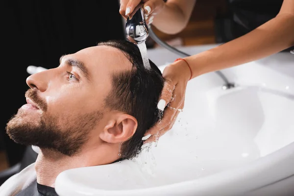 Coiffeur laver les cheveux de jeune client barbu dans le salon de coiffure — Photo de stock
