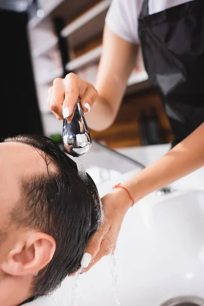 Visão cortada de barbeiro lavar o cabelo do cliente no salão de beleza — Fotografia de Stock