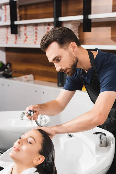 Young bearded barber washing hair of woman in beauty salon — Stock Photo