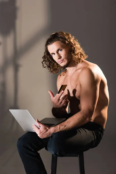 Сексуальный мужчина без рубашки с ноутбуком и кредитной картой — стоковое фото