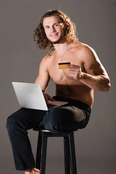 Sonriente sexy hombre sin camisa con ordenador portátil y tarjeta de crédito - foto de stock