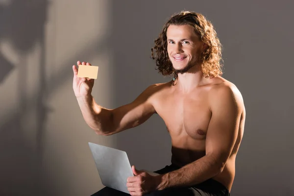Sonriente sexy hombre sin camisa con ordenador portátil y tarjeta de crédito - foto de stock