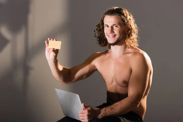 Smiling sexy shirtless man with laptop and credit card — Stock Photo