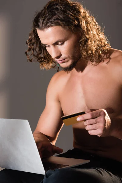 Sexy uomo senza maglietta in possesso di laptop e carta di credito — Foto stock