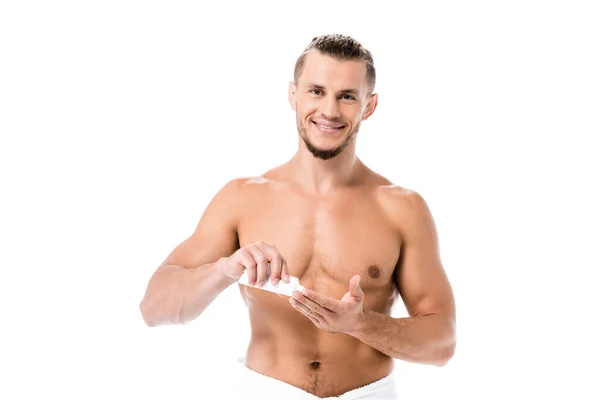 Усміхнений сексуальний без сорочки чоловік в рушнику наносить крем для рук ізольований на білому — стокове фото