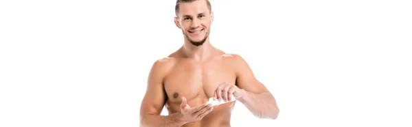 Uomo sexy senza maglietta sorridente in asciugamano applicando crema per le mani isolata su bianco, banner — Foto stock