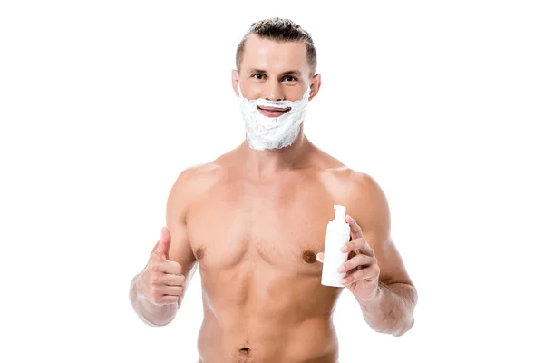 Sonriente sexy hombre sin camisa sosteniendo espuma de afeitar y mostrando el pulgar hacia arriba aislado en blanco - foto de stock