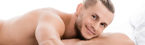 Lächelnd sexy hemdloser Mann posiert im Bett isoliert auf weißem Banner — Stockfoto