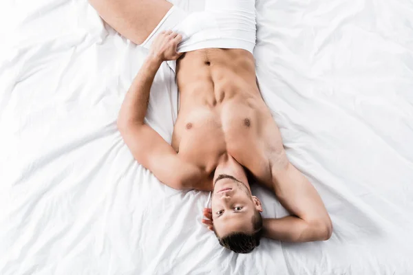 Vue de dessus de sexy homme torse nu posant dans le lit — Photo de stock