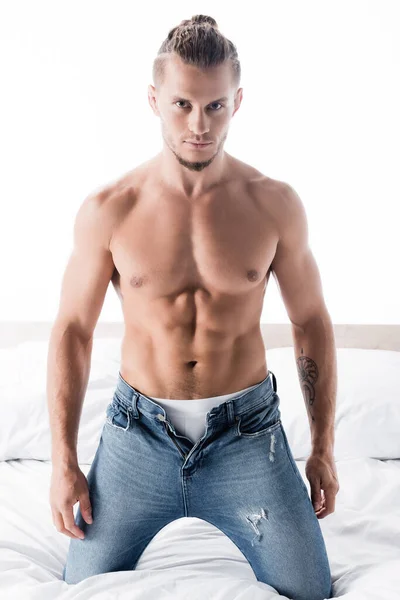 Сексуальный мужчина без рубашки в джинсах позирует в постели изолированы на белом — стоковое фото