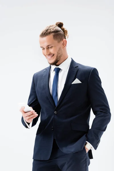 Улыбающийся молодой бизнесмен в костюме со смартфоном, изолированным на белом — стоковое фото