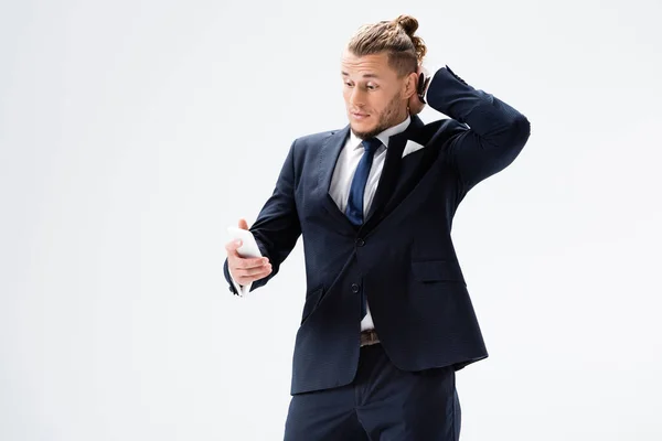 Confused young businessman in suit with smartphone isolated on white — Stock Photo